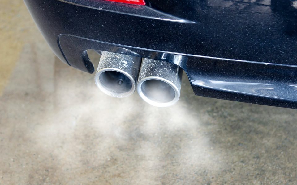 Exhaust smoke coming from the twin tailpipes of a dark car