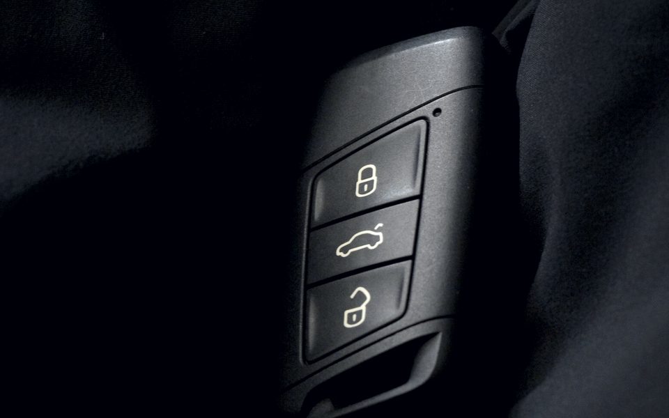 A modern car key fob with lock, boot and unlock buttons, resting on dark fabric