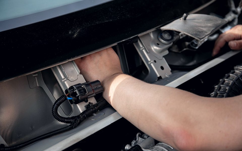 A technician reaching into a car to release a multi-pin electrical connector on a wiring loom
