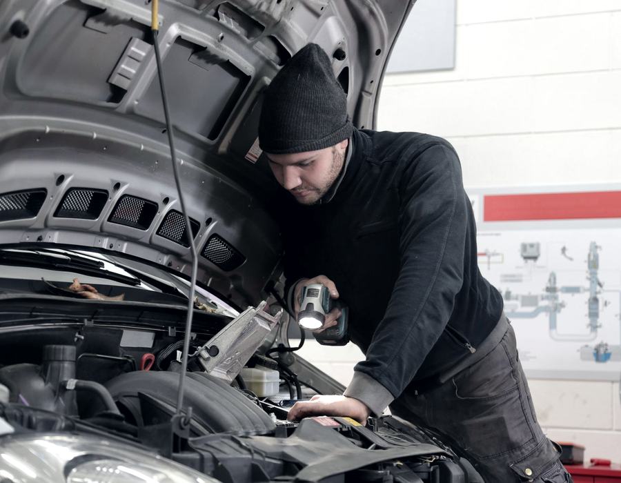 Technician inspecting an engine under the bonnet with a work lamp