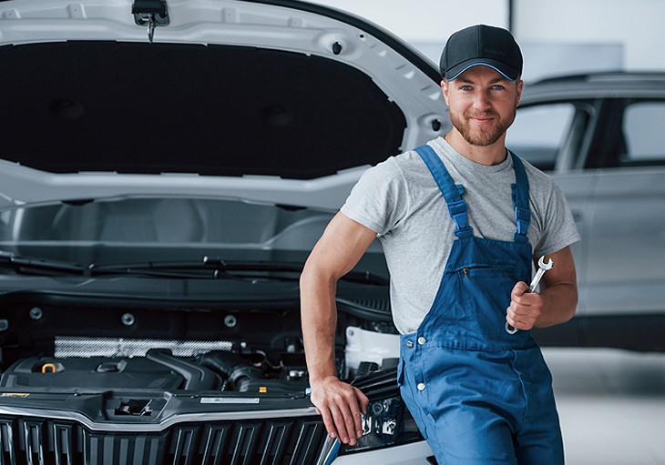 Technician standing beside a vehicle with the bonnet raised in a workshop